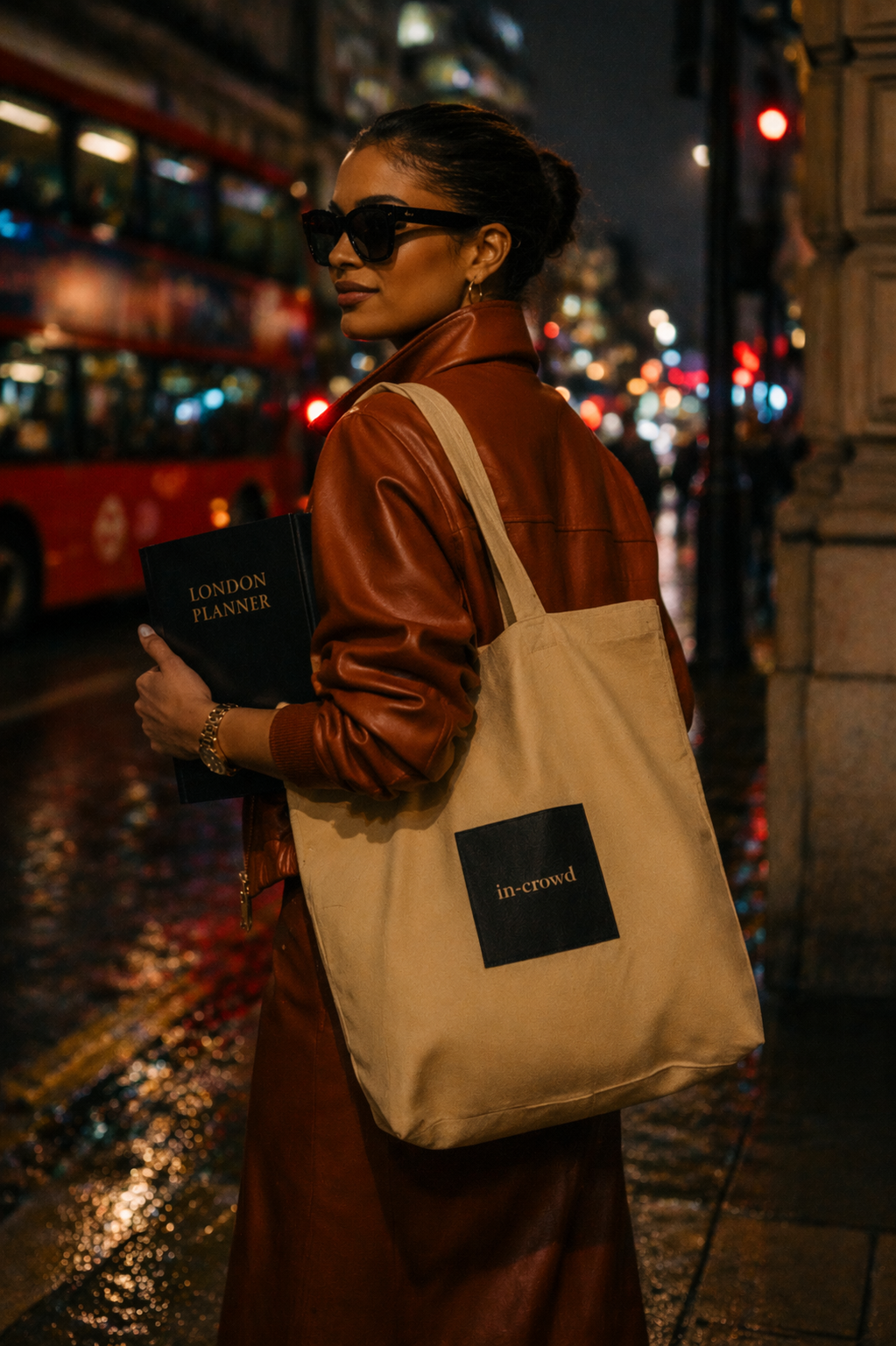 Woman holding a tote bag with 'In Crowd' branding on a city street at night.
