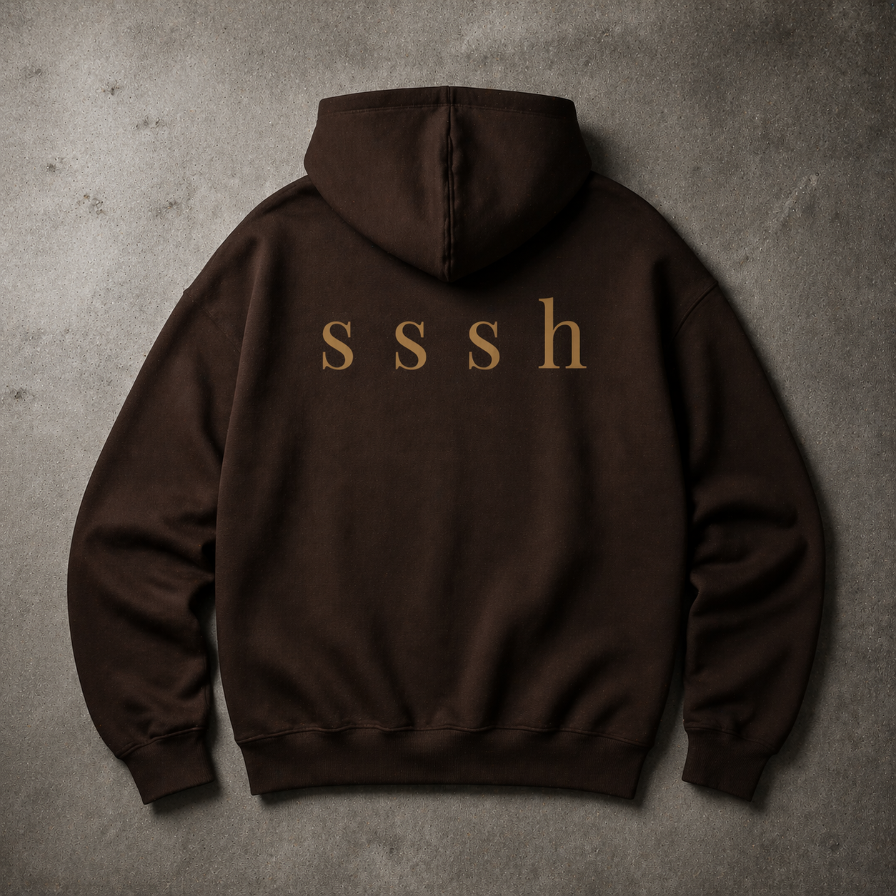 Brown hoodie with 'sssh' text on the back against a gray concrete background