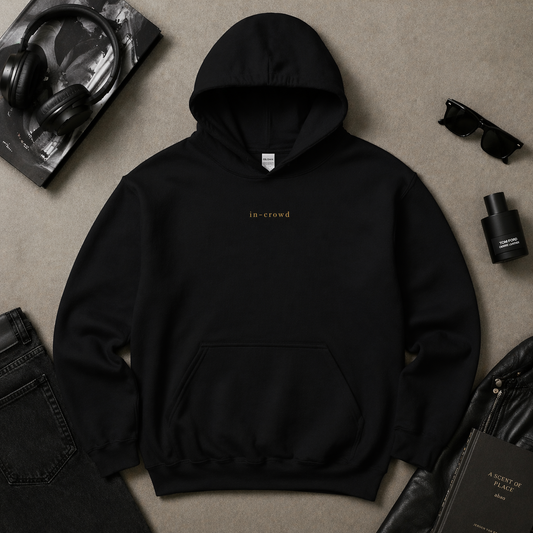 Black hoodie with 'in-crowd' text on a beige surface with accessories.