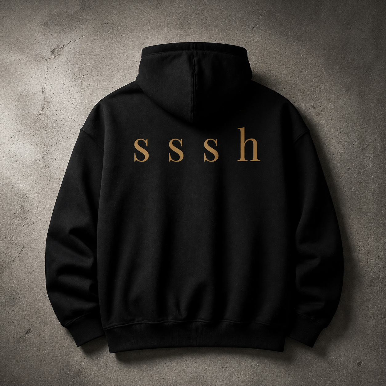 Black hoodie with 'sssh' text on the back against a concrete wall.