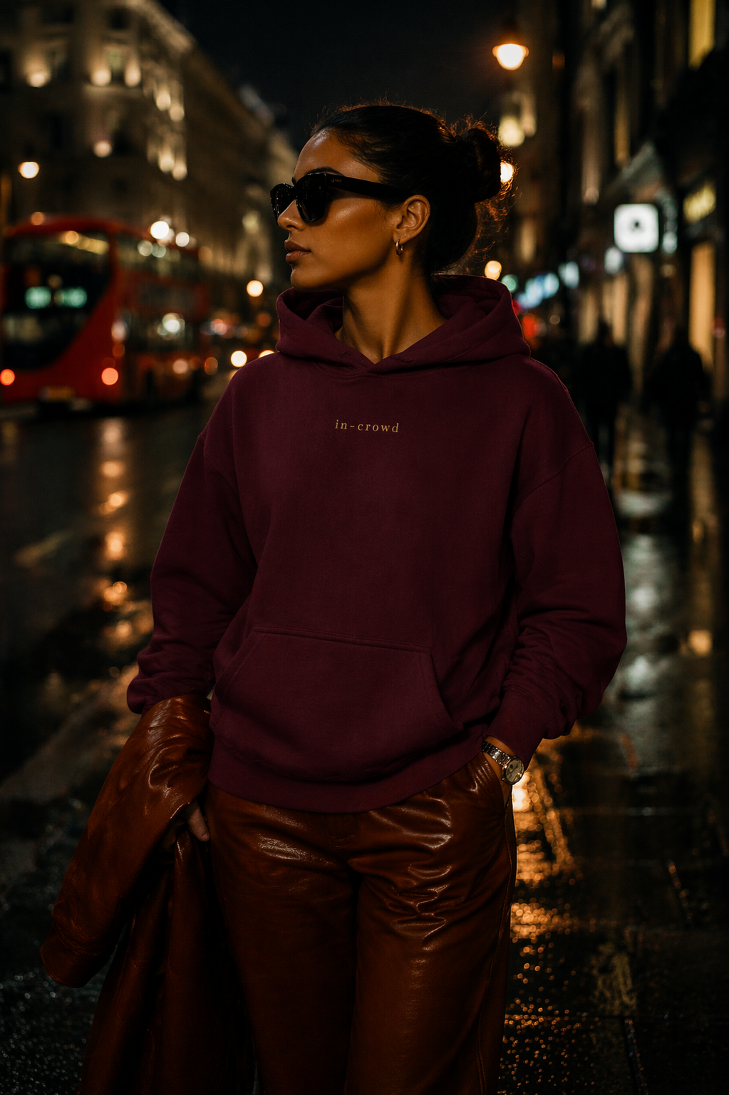 Person wearing a maroon hoodie and sunglasses on a city street at night.