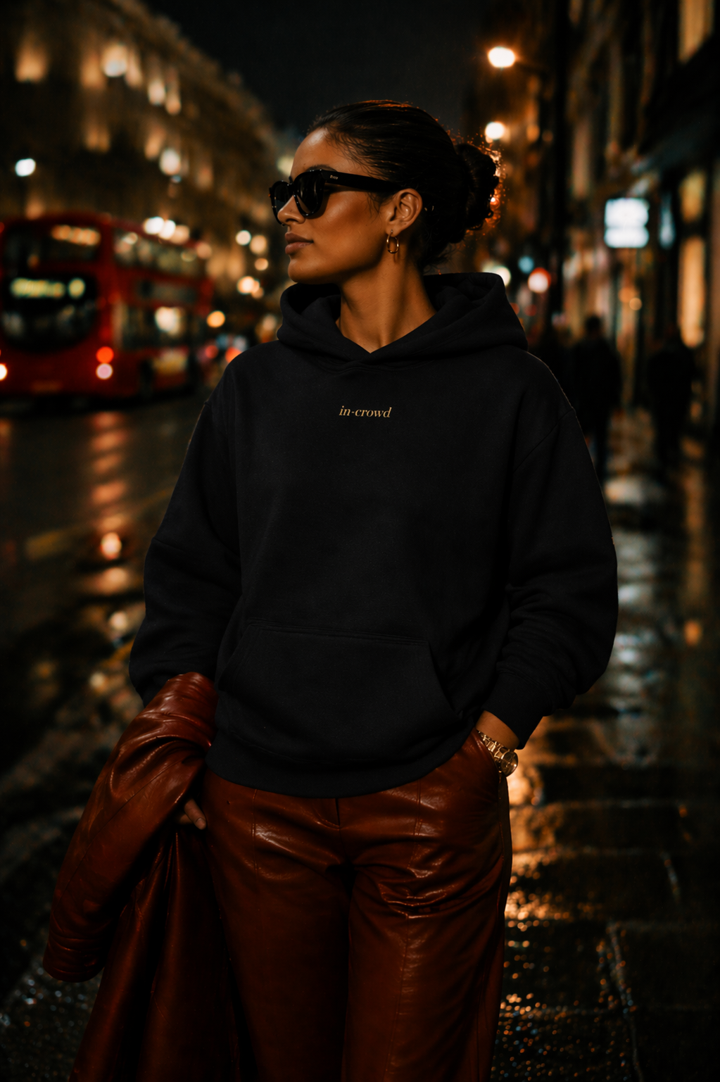Person wearing a black hoodie and brown leather pants on a city street at night.